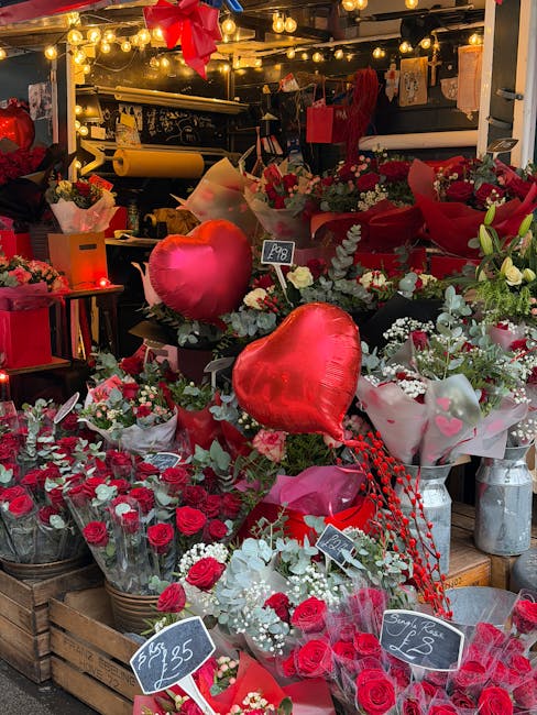 An indoor flower shop displays a vibrant assortment of floral arrangements and bouquets in shades of red, pink, and white, featuring roses, eucalyptus, and other seasonal blooms. The arrangement inclu