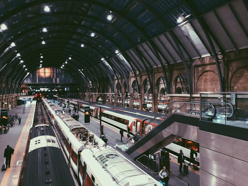Inside a large, historic train station with a high, curved glass and steel roof illuminated by internal lighting. The station features multiple train platforms with modern UK trains, some with white a