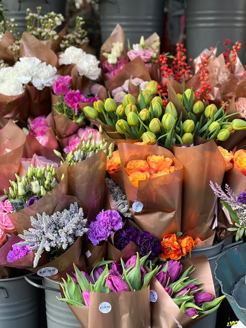 An assortment of fresh flowers displayed in metal containers at a floral shop, including white hydrangeas and purple carnations arranged on the left, with pink tulips in the front and orange roses tow